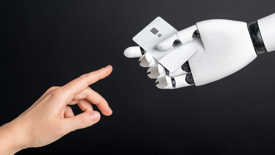Human-like black and white robot hand holding plastic credit or debit card and human hand on black background. AI and finance concept Human-like black and white robot hand holding plastic credit or debit card and human hand on black background. AI and finance concept