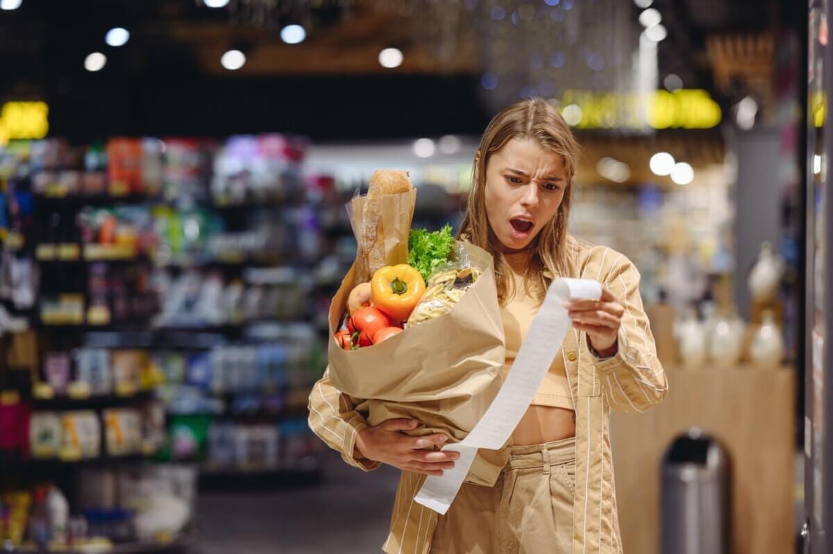 Young sad customer reads bill holding brown paper bag shopping at supermarket Young sad customer reads bill holding brown paper bag shopping at supermarket