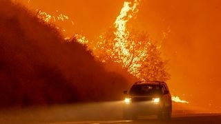 A car driving by a raging wildfire A car driving by a raging wildfire