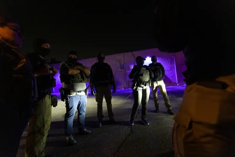 A group of officers standing in a parking lot at night wearing tactical vests and masks. A group of officers standing in a parking lot at night wearing tactical vests and masks.