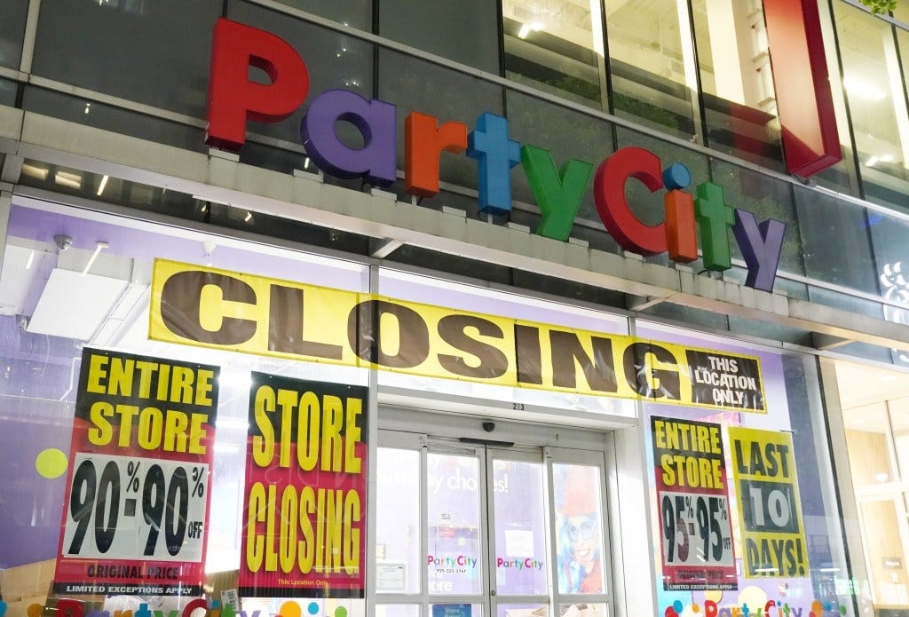 The exterior of a Party City store with "CLOSING" banners and sale signs, advertising discounts of 90-95% off. The exterior of a Party City store with "CLOSING" banners and sale signs, advertising discounts of 90-95% off.
