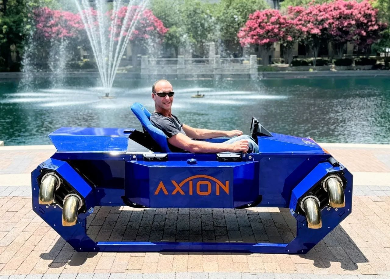 A man sits in the Axion personal vertical takeoff and landing vehicle from FusionFlight. The vehicle is blue A man sits in the Axion personal vertical takeoff and landing vehicle from FusionFlight. The vehicle is blue